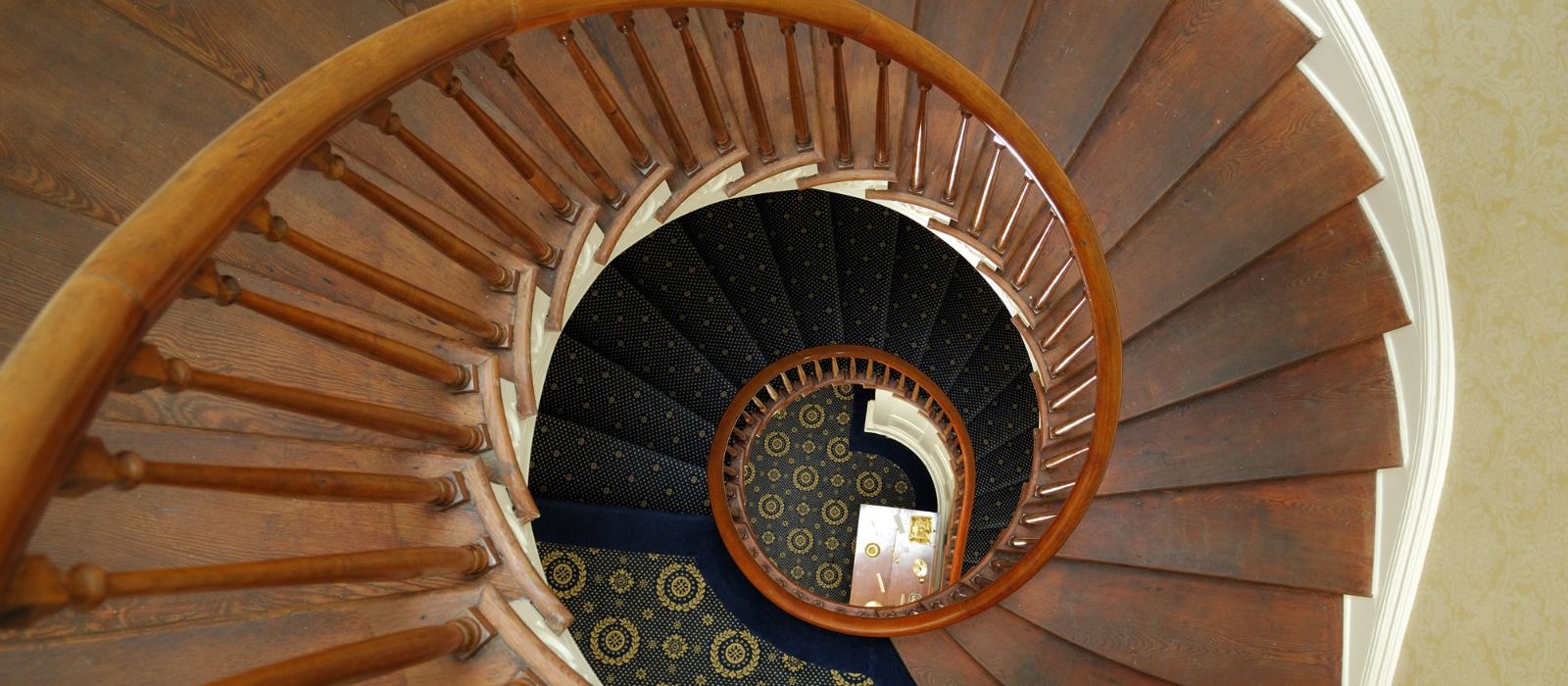 A cantilevered spiral staircase curving upward through three floors toward a glass cupola